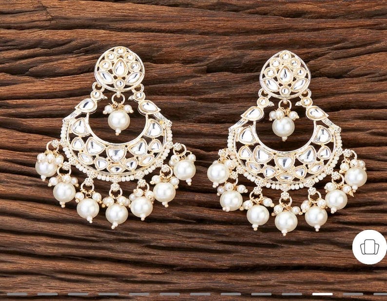 May include: A pair of gold-toned chandelier earrings with a floral design. The earrings feature a large, teardrop-shaped pearl at the bottom and smaller pearls dangling from the bottom. The earrings have a detailed, ornate design with clear, reflective accents.