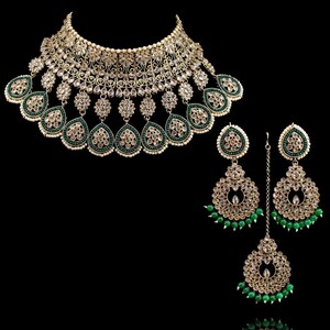 May include: A gold and green Indian bridal necklace set with a large, ornate choker, matching earrings, and a maang tikka. The necklace features intricate designs with clear stones and green beads.