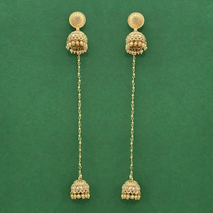 May include: A pair of gold-colored earrings with a dangling design. Each earring features a circular top with a central design, a bell-shaped body, and a chain of small beads connecting to a smaller bell-shaped bottom. The background is a solid green.