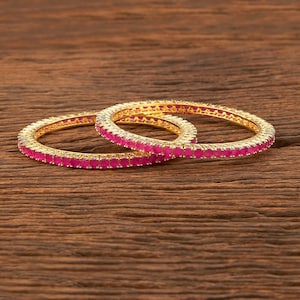 May include: Two gold bangles with pink gemstones set in a circular pattern.