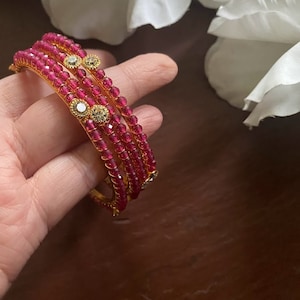 Könnte beinhalten: Set aus vier rosafarbenen Perlenarmbändern mit goldenen Akzenten und klaren Strasssteinen.