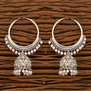 May include: A pair of silver hoop earrings with pearl accents and a dangling jhumka design. The jhumkas are adorned with clear stones.