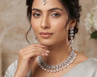 May include: A woman wearing a silver necklace, earrings, and headpiece with pearl accents. The jewelry has a leaf design. A gold pin with the word "Era" is on the woman's clothing.