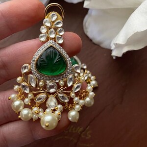 May include: Gold earrings with a green gemstone, white stones, and pearl accents.