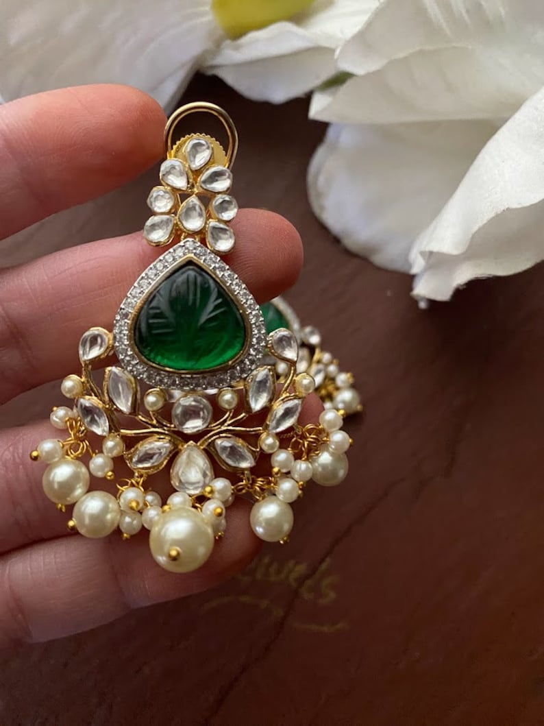 May include: Gold earrings with a green gemstone, white stones, and pearl accents.