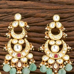 May include: Gold-toned earrings with a crescent moon design, featuring clear and red accents, and teardrop-shaped green gemstones. The earrings have a detailed, ornate design with small pearl-like embellishments.
