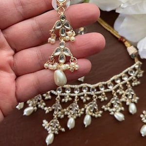 May include: A gold necklace with a delicate design featuring white pearls and clear stones. The necklace has a matching pair of earrings with a similar design.