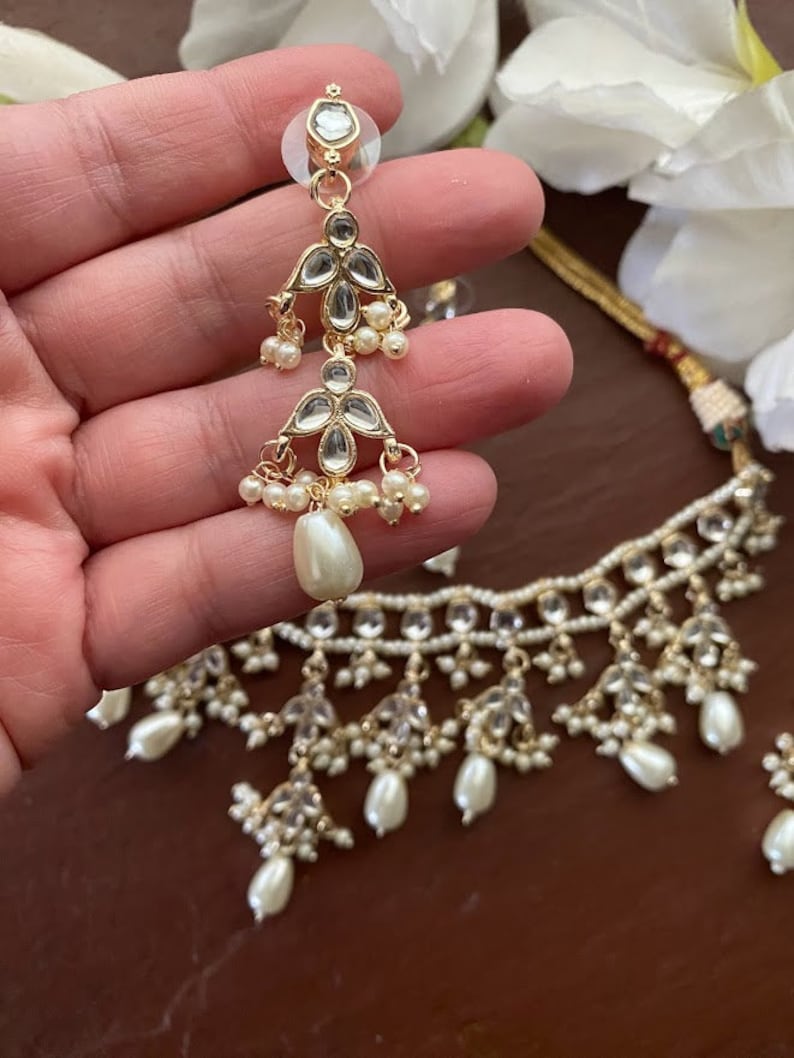 May include: A gold necklace with a delicate design featuring white pearls and clear stones. The necklace has a matching pair of earrings with a similar design.