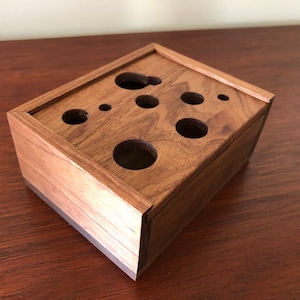 May include: A wooden box with a dark brown finish and a rectangular shape. The box has a lid and several circular cutouts on the top.