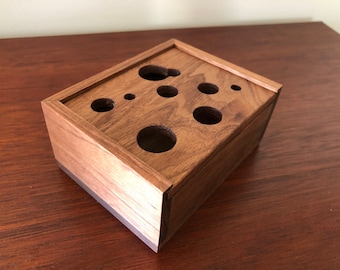 May include: A wooden box with a dark brown finish and a rectangular shape. The box has a lid and several circular cutouts on the top.