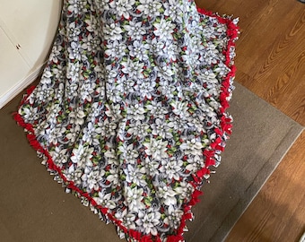 Könnte beinhalten: Eine graue und weiße Fleece-Decke mit rotem Saum und einem Weihnachtsstern-Muster. Die Decke ist gefaltet und über einen Stuhl gelegt.