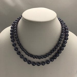 May include: A double strand necklace made of dark purple beads. The necklace is displayed on a white mannequin bust.