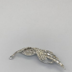 May include: A silver tone brooch with a swirling design set with clear rhinestones.