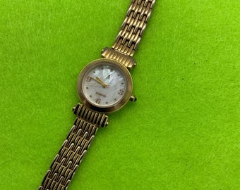 May include: A gold-toned wristwatch with a white face and a gold metal band. The watch face has black hour and minute hands and a small second hand. The watch face also has black Roman numeral hour markers.