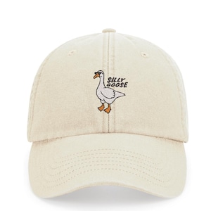 Peut inclure: Une casquette de baseball en coton beige avec une oie blanche brodée portant des lunettes de soleil et le texte "Silly Goose".