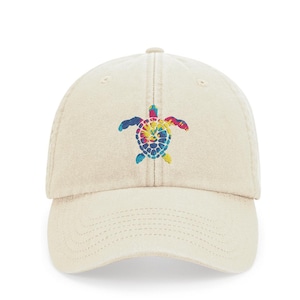Pode incluir: Um boné de beisebol bege com um design de tartaruga marinha tie-dye bordado. A tartaruga está em tons de azul, verde, amarelo, laranja e rosa.