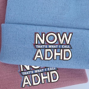 May include: Two knitted beanies, one light blue and one dusty rose, are shown. The light blue beanie features the embroidered text "NOW THAT'S WHAT I CALL ADHD". A pink tag with "KC studios" is attached to the blue beanie.