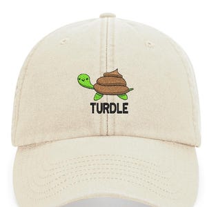 May include: A beige baseball cap with an embroidered green turtle carrying a brown pile of poop. The text "TURDLE" is embroidered below the turtle.