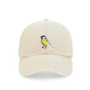 May include: A beige baseball cap with an embroidered bluebird design. The bird is yellow with blue wings and a black eye.