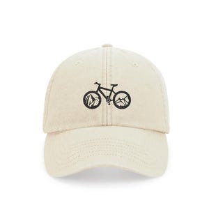 May include: A beige baseball cap with a black embroidered mountain bike design. The bike has mountains in the wheels.