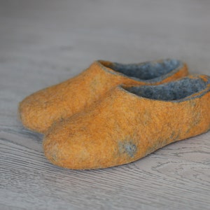 Könnte beinhalten: Ein Paar gelbe Filzpantoffeln mit grauer Filzfutter. Die Pantoffeln sind weich und gemütlich, perfekt um die Füße im Winter warm zu halten.
