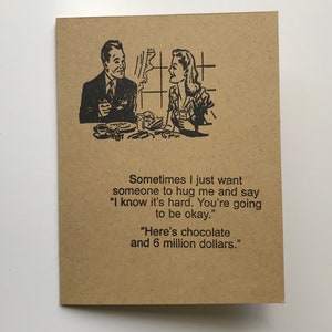 May include: A brown card with a black and white illustration of a couple sitting at a table. The text on the card reads: "Sometimes I just want someone to hug me and say "I know it's hard. You're going to be okay." "Here's chocolate and 6 million dollars."