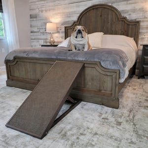 May include: A dark brown pet ramp with a textured, non-slip surface and an adjustable folding frame. The ramp is positioned at an angle in front of a wooden bed frame, featuring a sloped design to assist pets in reaching elevated surfaces.