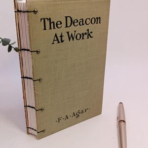 May include: A green linen-bound book with the title "The Deacon At Work" and the author's name "F.A. Agar." printed on the cover.