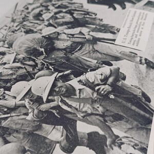 May include: A monochrome photograph showing soldiers in a war scene, wearing helmets and uniforms. The image is from a historical document, with text visible in the upper right corner. The photograph is a close-up, showing the soldiers in a chaotic scene.