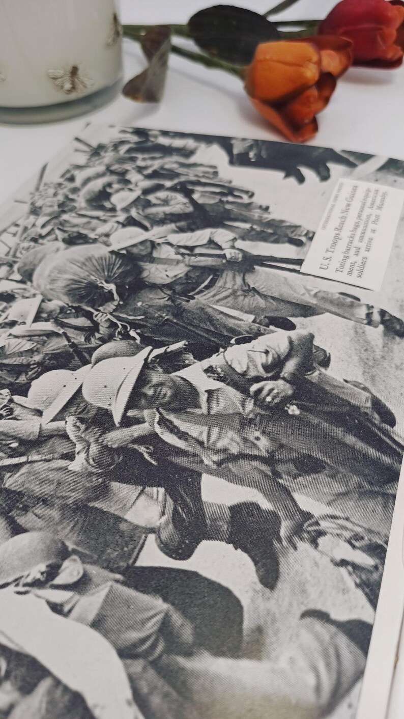 May include: A monochrome photograph showing soldiers in a war scene, wearing helmets and uniforms. The image is from a historical document, with text visible in the upper right corner. The photograph is a close-up, showing the soldiers in a chaotic scene.