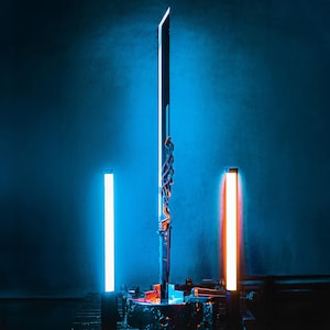 Puede incluir: Una espada futurista con una hoja larga y recta, iluminada por una luz azul brillante. La empuñadura presenta un cableado intrincado y detalles en naranja. La espada se exhibe sobre una base metálica, con luces de neón verticales a cada lado.