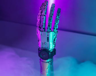 May include: A silver robotic hand with a black wristwatch. The hand is raised with four fingers extended and the thumb tucked in. The background is a gradient of purple and blue.