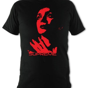 Op de afbeelding: Zwart T-shirt met een rood silhouet van een vrouwenhoofd en een hand, met daaronder het woord "SUPREME" gedrukt.