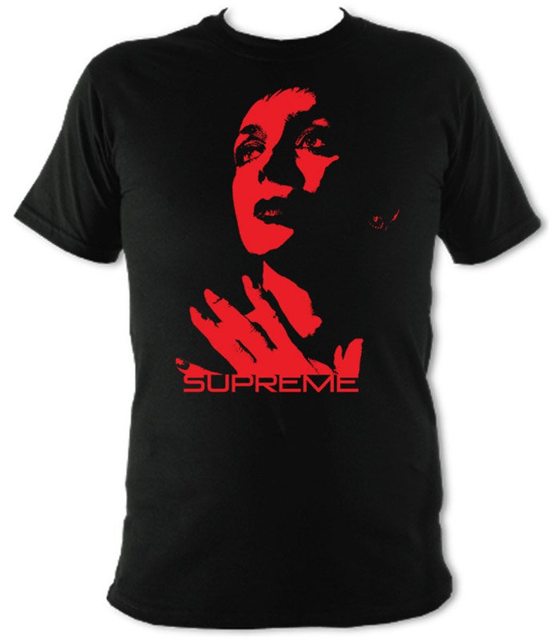 Op de afbeelding: Zwart T-shirt met een rood silhouet van een vrouwenhoofd en een hand, met daaronder het woord "SUPREME" gedrukt.