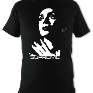 Op de afbeelding: Zwart T-shirt met een wit silhouet van een vrouwenhoofd en handen, met het woord "SUPREME" eronder gedrukt.