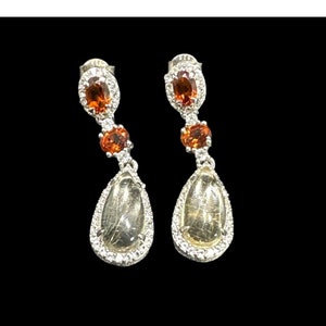 May include: A pair of silver dangle earrings with a teardrop-shaped clear stone and two smaller orange stones.
