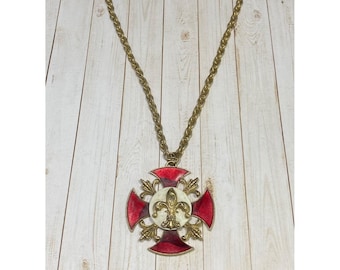 Könnte beinhalten: Eine goldene Kettenkette mit einem großen Anhänger. Der Anhänger ist ein rotes und weißes Emaille-Kreuz mit einer goldenen Fleur-de-lis in der Mitte.