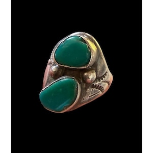 May include: A silver ring featuring two large, oval-shaped turquoise stones. The ring has a detailed, textured design around the stones and on the band. The turquoise stones are a vibrant green color, set in a silver metal.