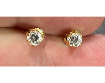 May include: A pair of gold stud earrings with small, clear round stones.