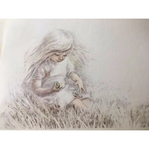 May include: A young girl with long blonde hair sits in a field of tall grass, holding a small green object in her hand. She is wearing a white dress and looking down at the object.
