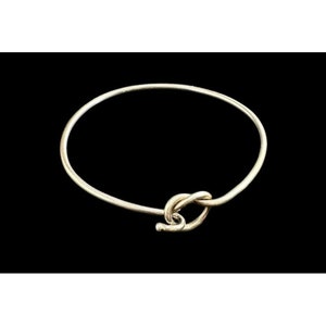 May include: A silver bangle bracelet with a knot design. The bracelet is open and has a simple, elegant style.