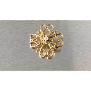 May include: A gold-toned brooch with a delicate, intricate design featuring a central pearl.