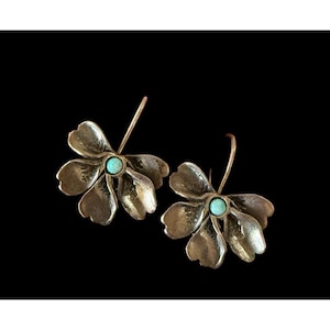 May include: A pair of flower-shaped earrings with a light teal center stone. The earrings are made of a gold-colored metal and have a hook closure. The petals of the flowers are detailed with subtle textures.