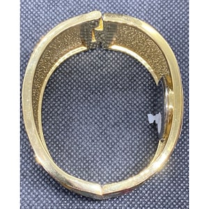 May include: A gold-toned bangle bracelet with a floral design. The bracelet is open and has a hinged clasp.