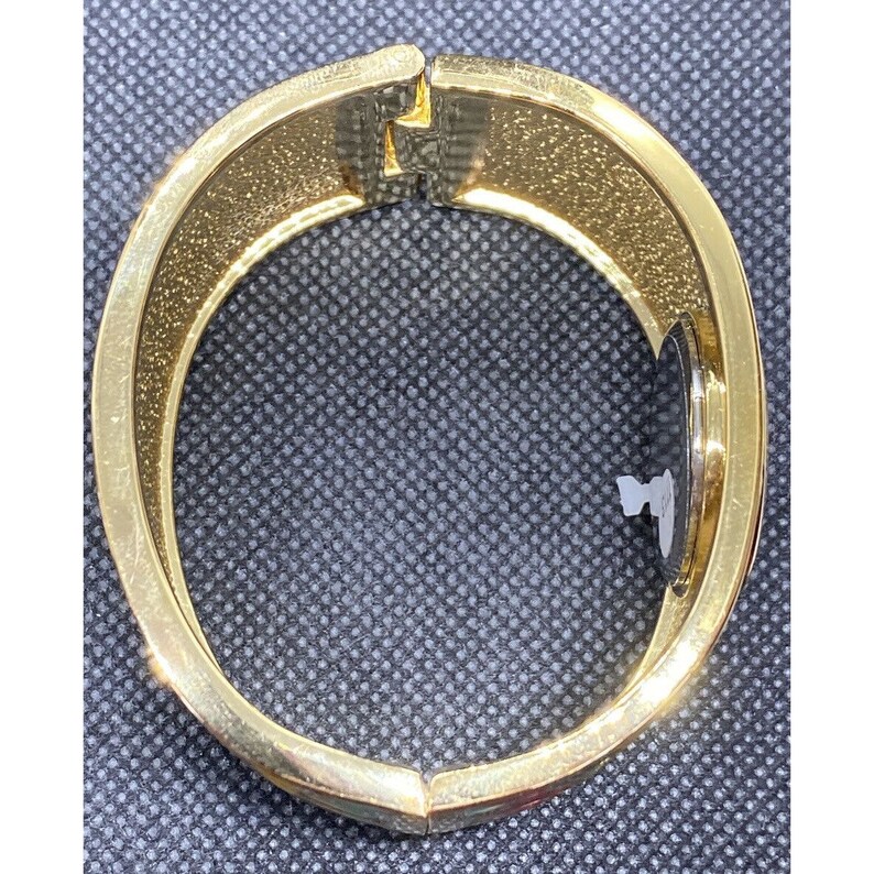 May include: A gold-toned bangle bracelet with a floral design. The bracelet is open and has a hinged clasp.