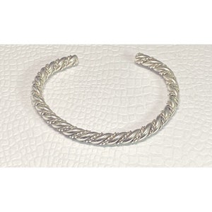 May include: A silver twisted bangle bracelet. The bracelet is made of a thick, twisted wire and has a smooth, polished finish.