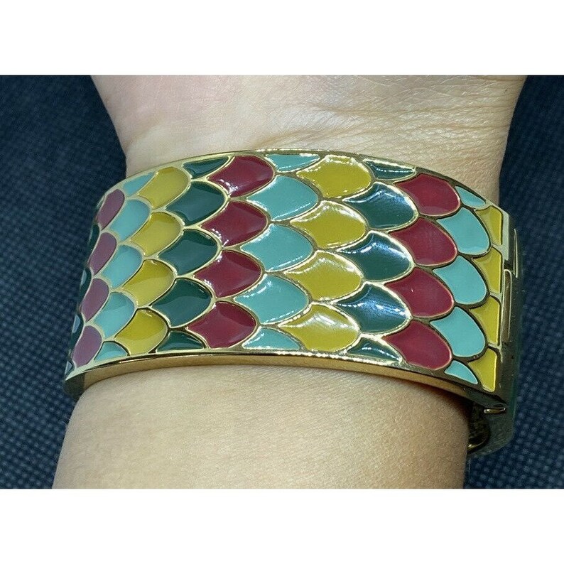 May include: A gold bangle bracelet with a colorful enamel design. The design features a repeating pattern of green, yellow, red, and blue scales.