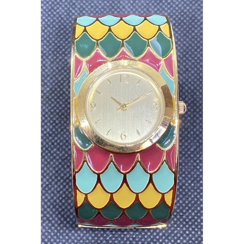 May include: A gold-tone wristwatch with a white face and black hands. The watch band is a colorful bangle with a pattern of green, yellow, and red scales.