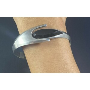 May include: A silver bracelet with a black stone set in a modern design.