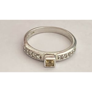 May include: A silver ring with a square-shaped center stone and a band of small clear stones.